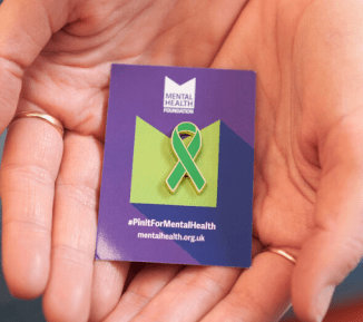 Someone holding a green ribbon pin badge